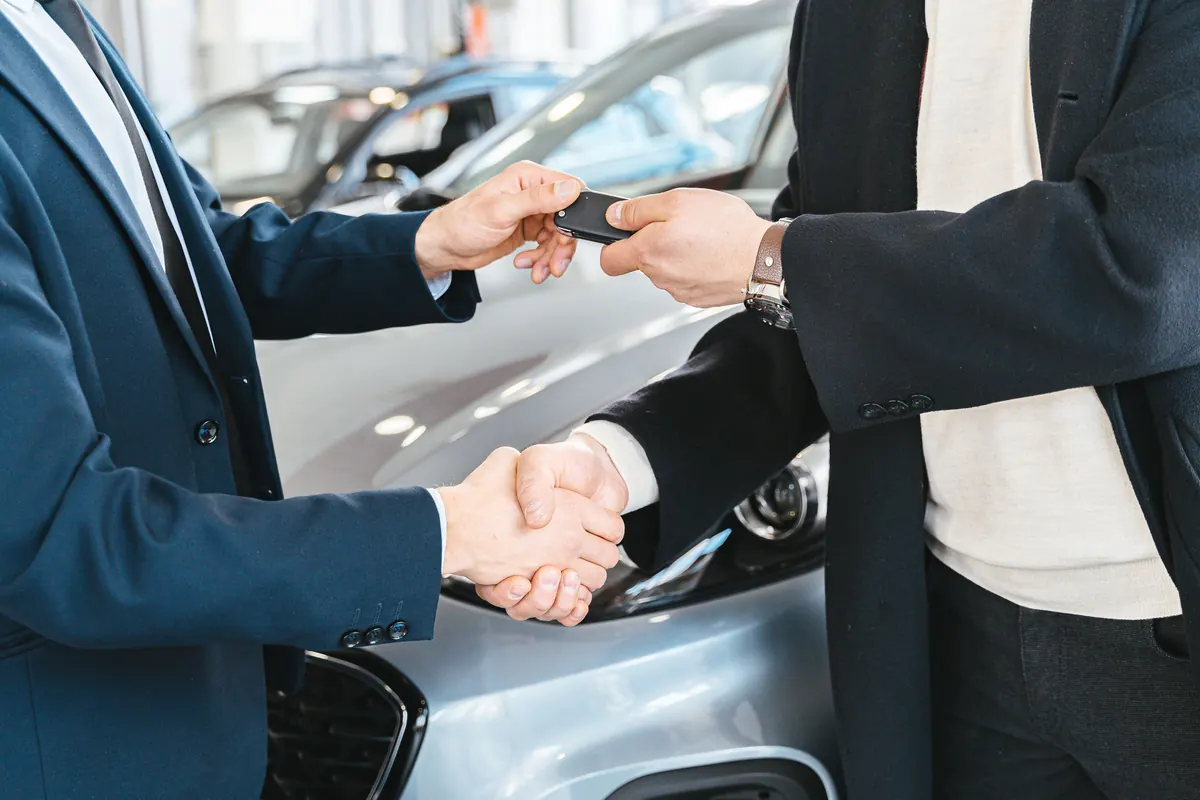 Handing over the keys with a handshake in front of a rental car