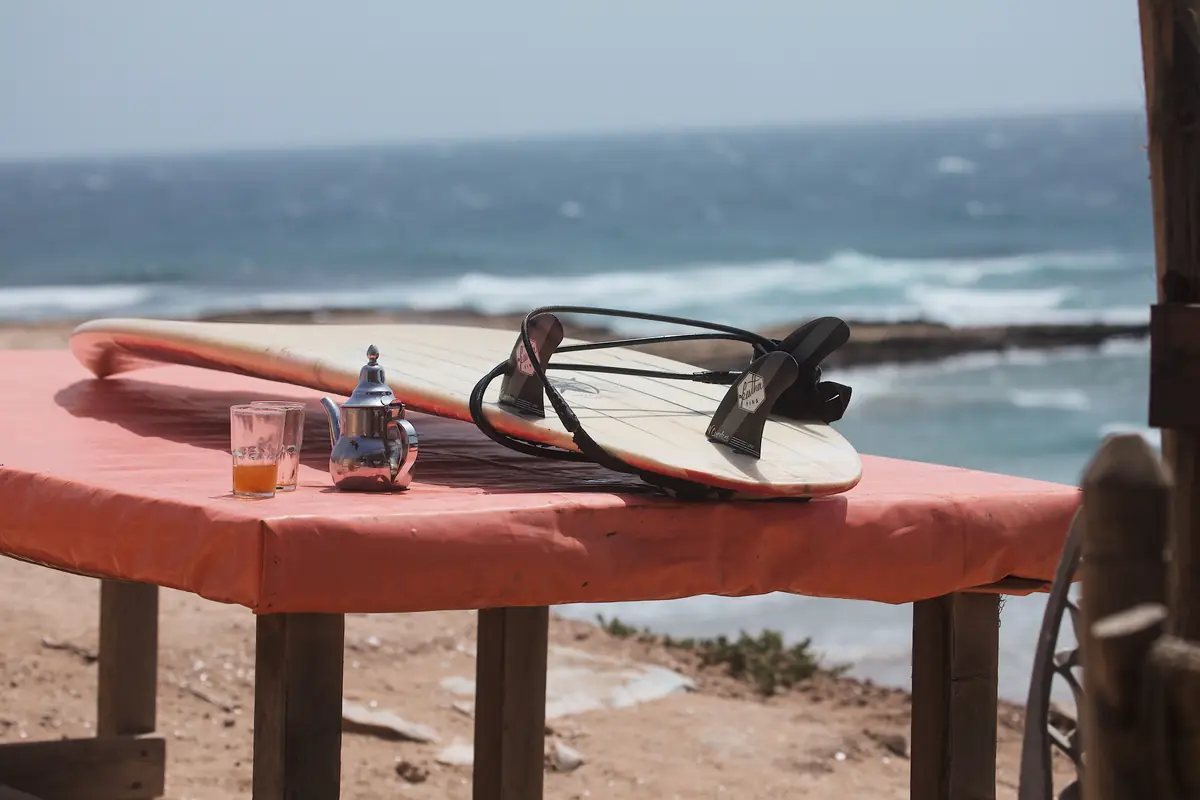 Surfboard and mint tea on a table facing the ocean